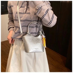 Détail du sac cabas argenté avec poignées cylindriques et breloque décorative en perles