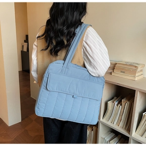 Detailansicht einer blauen gesteppten Tragetasche mit Vordertasche an der Schulter
