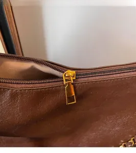 Close-up of smooth gold metal zipper and textured dark brown leather tote bag