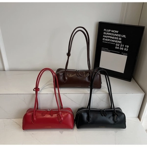 Three minimalist cylindrical leather bags in red, brown, and black on marble surface