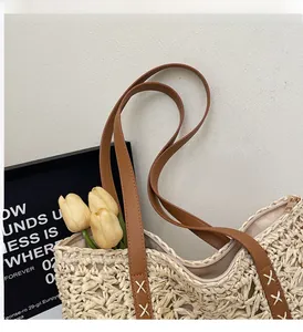 Detail of woven straw tote bag with brown leather strap and white cross-stitch craftsmanship