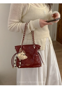 Close-up of wine red quilted bucket bag with chain strap and cute bear charm pendant