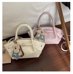 Detail view of stylish cream and pink bucket bags with cute bear charms on wood floor