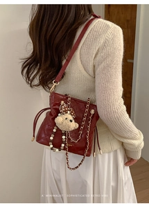 Detail of burgundy quilted leather bucket bag with gold chain strap and bear charm