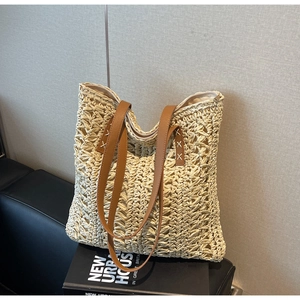 Close-up of woven straw tote bag with brown leather handles on a leather background