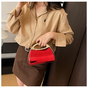 Close-up of red glossy acrylic clutch bag with golden metal handle and chain strap