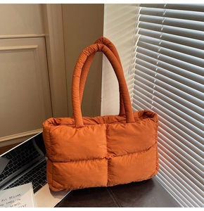Detail of the orange quilted puffer tote bag on a desk near a laptop computer