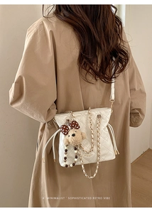 Close-up of quilted white bucket bag with chain strap and cute bear charm detail