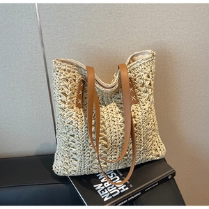 Detail of hand-stitched X-pattern on brown leather straps of a cream woven tote bag