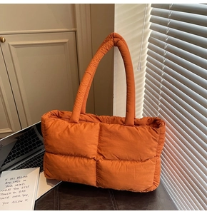 Detail shot of bright orange quilted puffer tote bag with thick handles in a cozy setting