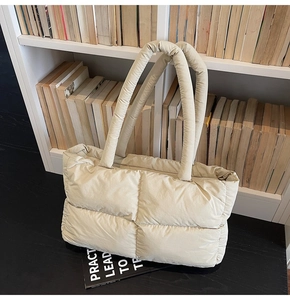 Close-up of beige quilted puffer tote bag with thick padded handles on a desk