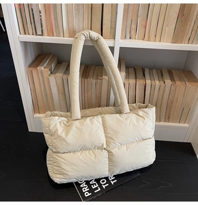 Close-up of cream white quilted puffer tote bag with thick padded handles on a black table