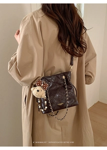 Detailed view of dark brown quilted leather bucket bag with gold chain and plush bear charm