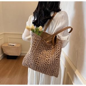 Rear view of a woven straw tote bag with brown leather straps worn by a model in a room
