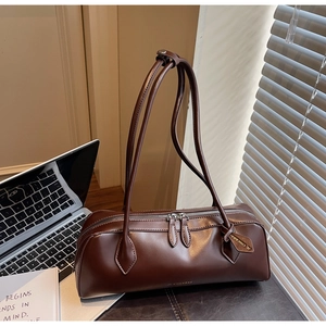 Detail of a dark brown baguette bag with double zipper and sleek synthetic leather texture