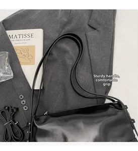 Detail of glossy black leather baguette bag with metal buckle and shoulder strap