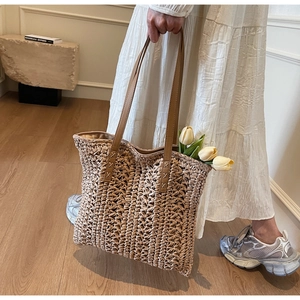 Close-up of woven straw tote bag featuring brown leather handles and cross-stitch detail