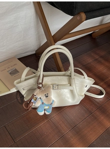 Chic cream bucket bag with silver buckles and a cute teddy bear charm on a wooden chair