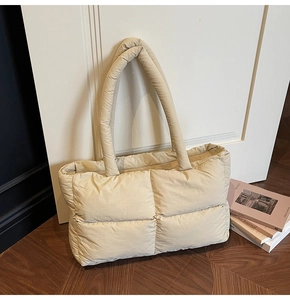 Detail of beige quilted puffer tote bag leaning against a white door on wooden floor