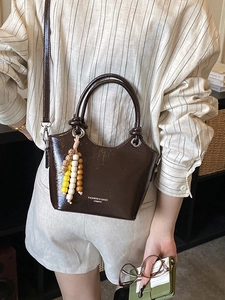 Sac seau en cuir verni marron foncé avec pompon en perles porté par un mannequin