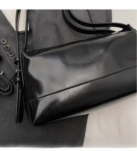 Close-up of black glossy patent leather shoulder bag on grey suit jacket showing smooth texture