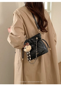 Quilted black bucket bag with gold chain strap and cute bear charm shown on model