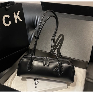 Detail of black cylindrical baguette bag with gold logo and dual zipper in a gift box