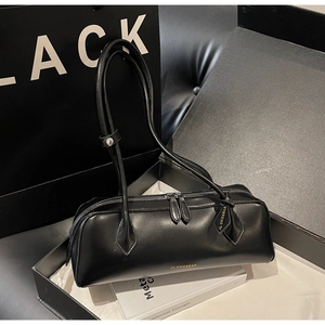 Detail view of black minimalist handbag with gold branding inside an elegant gift box