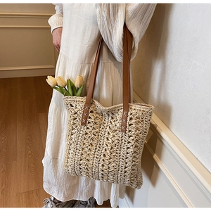 Detail of straw tote bag showing brown leather straps with white cross stitching