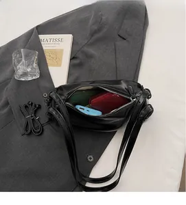 Flat lay of black leather baguette bag showing spacious interior with red lining and items