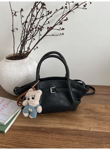 Close-up of black bucket bag with silver buckle, leather texture, and cute bear charm