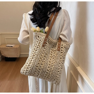 Detail of hand-woven straw tote with brown leather straps and intricate crochet pattern