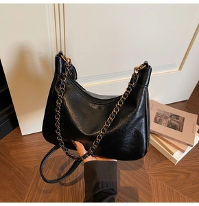 Detail view of black crescent tote bag featuring glossy wrinkled leather and dual straps