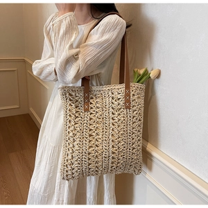 Detailed view of the woven straw tote bag with brown leather straps and X-stitch sewing