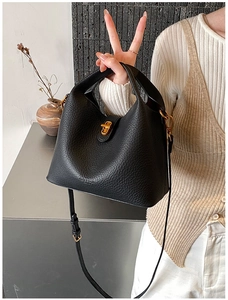 Détail du sac seau en cuir noir grainé avec fermoir doré porté par un mannequin