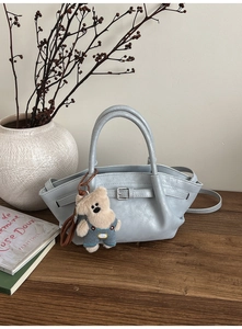 Detail of light blue leather bucket bag with plush bear charm and metallic ring decor
