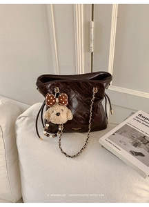 Detail of dark brown quilted leather bucket bag with plush bear charm and gold chain