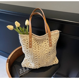 Detail of hand-woven hollow straw tote bag with brown leather handles and 'X' stitching