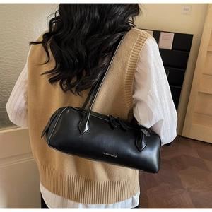 Detail of minimalist black leather baguette bag with elegant gold logo on beige outfit