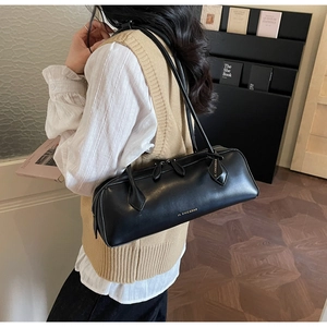 Close-up of black leather cylinder shoulder bag with gold branding and long straps