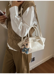 Detail of cream bucket bag with decorative strap and cute teddy bear plush charm accessory