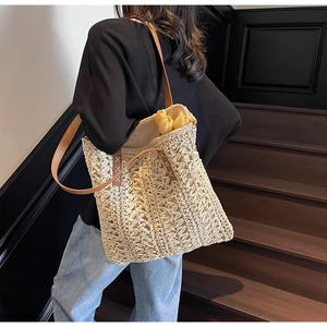Detail of woven straw tote bag featuring brown leather straps and white X-stitch detail