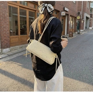 Détail du sac baguette blanc cassé avec imprimés étoiles grises et lanières sur le côté