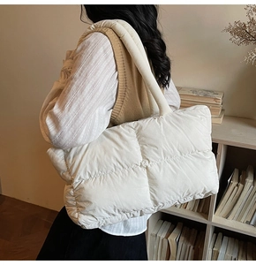 Lifestyle shot of an oversized off-white quilted puffer tote bag on a model shoulder