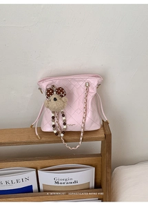 Detailed close-up of pink quilted bucket bag with golden chain strap and plush bear charm