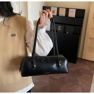 Detail of minimalist black leather baguette bag with golden logo and silver zipper