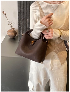 Détail du sac seau en cuir marron foncé montrant le grain de litchi et le fermoir doré