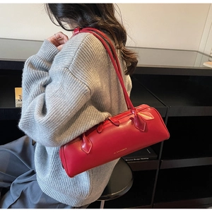 Detail view of the red sausage baguette bag with gold logo on a model with grey sweater