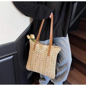 Close-up of handmade straw tote bag featuring brown leather straps and cross-stitch detail