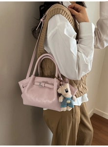 Pink leather bucket bag with teddy bear charm shown on a shoulder in a lifestyle setting